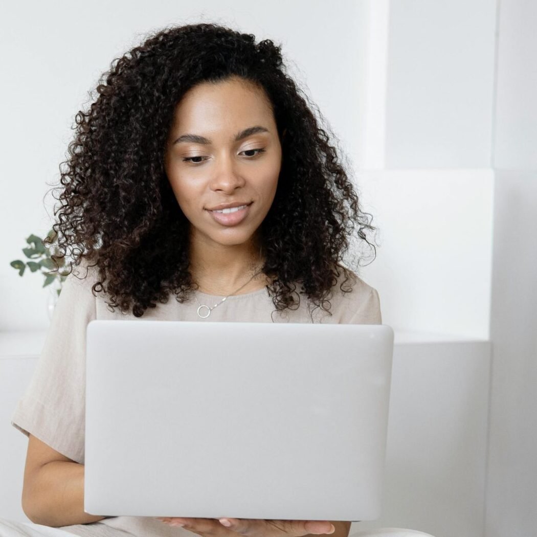 Young woman with curly hair working on her laptop in a cozy home setting, exuding confidence and focus.